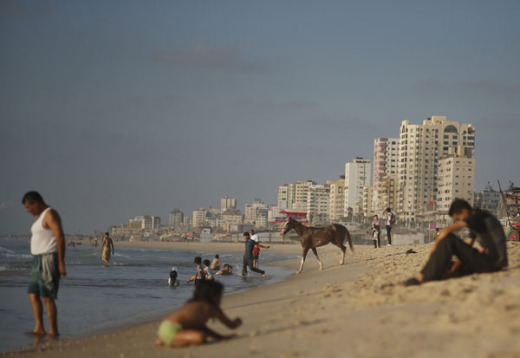 A Palestinian man leads a horse to the sea others sit on the beach in Gaza City